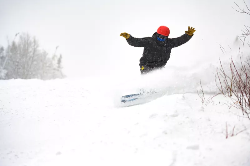 A snowboarder in a black snowsuit hits a powder stash on a snowy day.