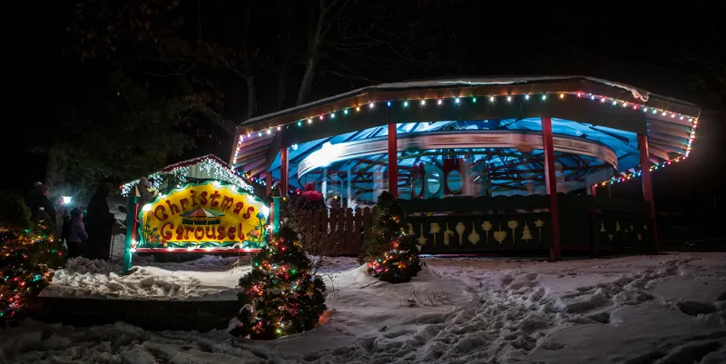 A Christmas carousel decorated with holiday lights at night.