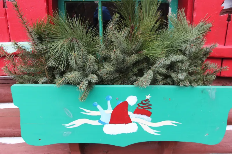A window box of fresh pine greenery features a painted Santa hat.