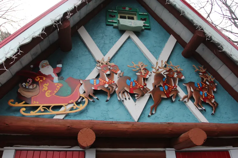 Wood reindeer and a Santa in his sleigh decorate a gingerbread trim building.
