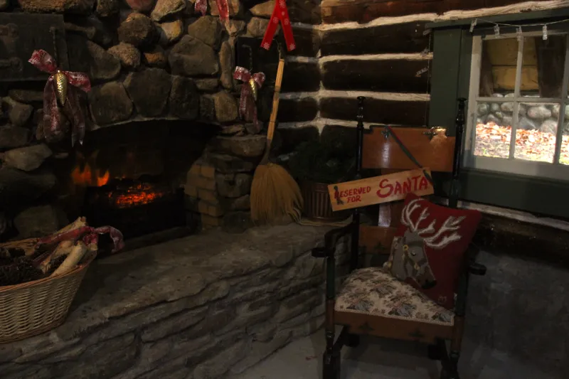 An antique wood chair sits next to a glowing stone fireplace. The chair has a sign on it that read "Reserved for Santa."