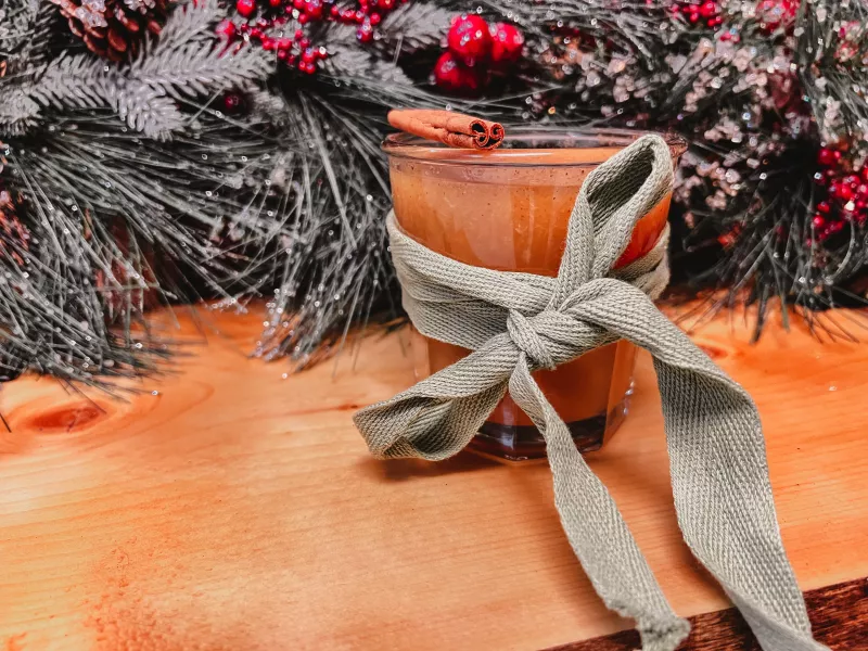 A light brown beverage with a holiday backdrop and green bow and cinnamon stick.