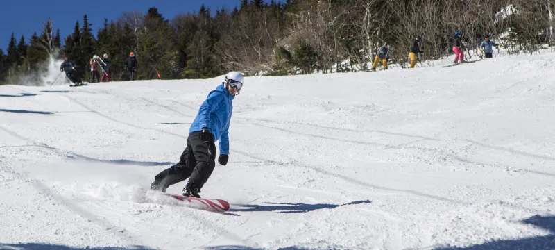A snowboarder with a blue jacket smoothly rides down a groomed trail.