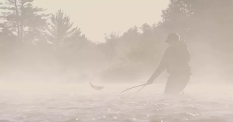 Evan Bottcher prepares his net as he reels in a fish on a misty morning in the Ausable River.