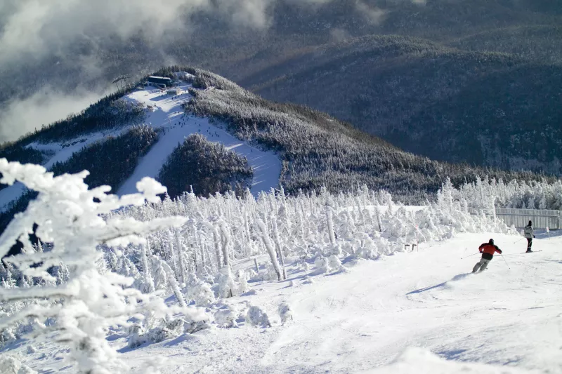 Little Whiteface's summit in the distance as skiers go down the trail in front of it.