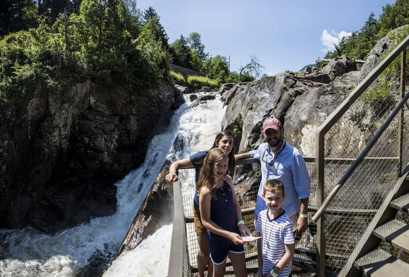 A family with two young kids poses in front of a waterfall at High Falls Gorge.