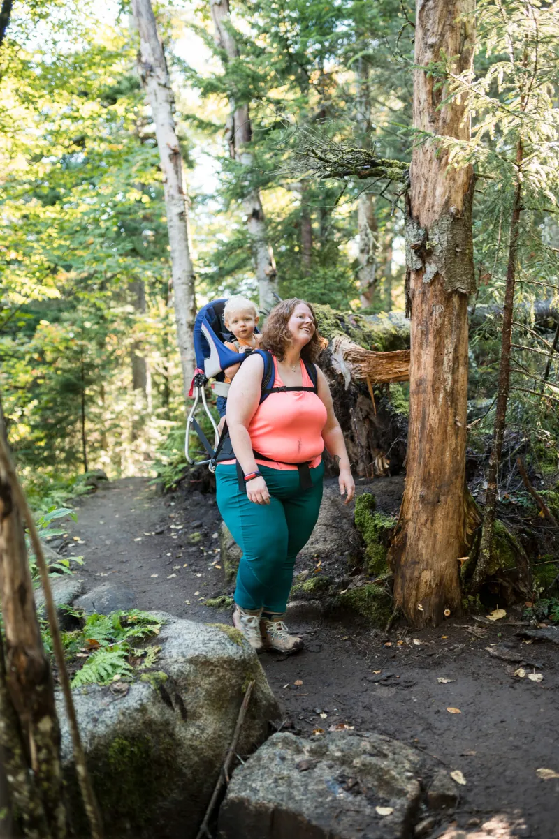 A mother hikes through the woods while carrying her son in a baby carrier backpack