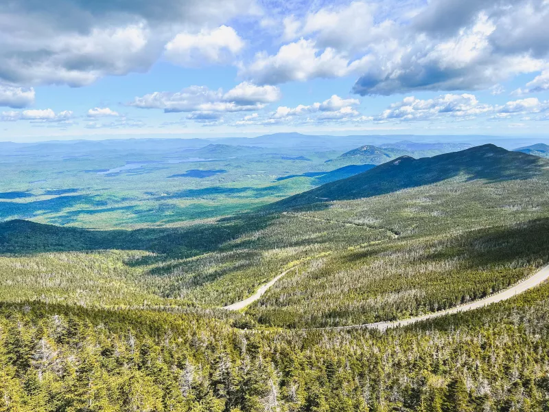 A view from a mountain in summer with forested mountains stretching into the distance.
