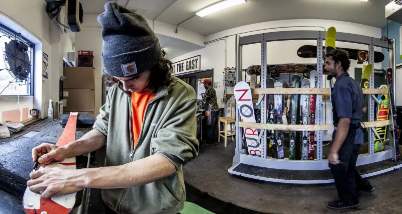A man works on tuning a ski in a repair shop.
