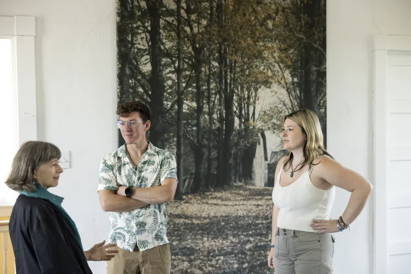 Three people talk in front of a large mural