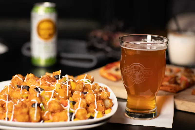 A close-up of tater tot nachos and a cool glass of golden beer.