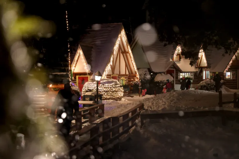 A festive Christmas village at night is bright with cheerful lights and snow.