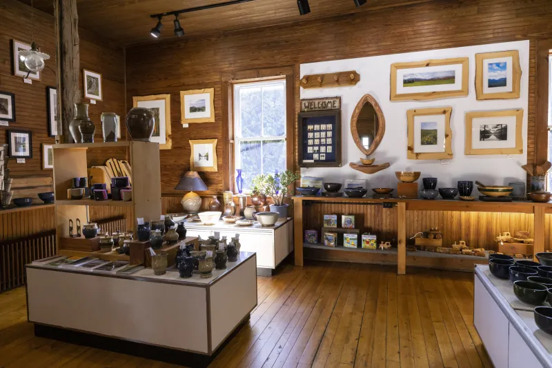A sunlit shop features handcrafted pottery, wood items, and framed photos.