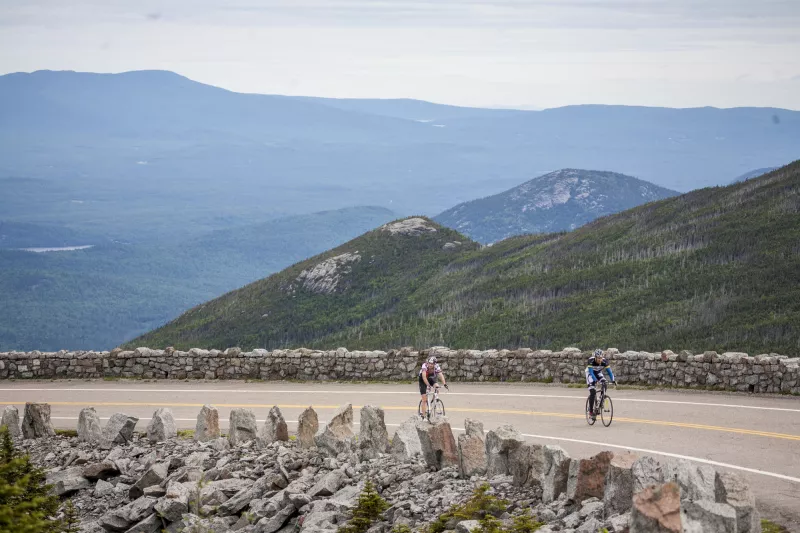 Two cyclists pedal uphill on the Whiteface Veterans' Memorial Highway with grand Adirondack views in the background