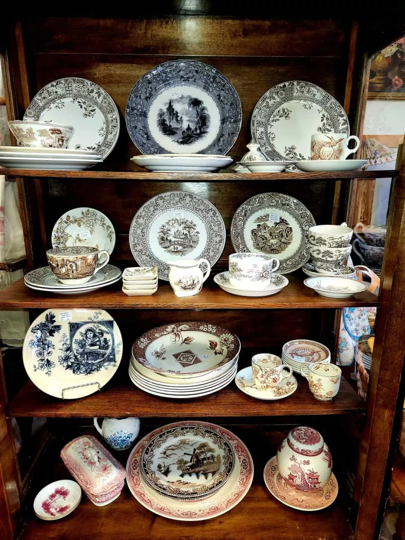 A wood china cabinet is filled with antique plates, cups, saucters, and more in a range of patterns and colors.