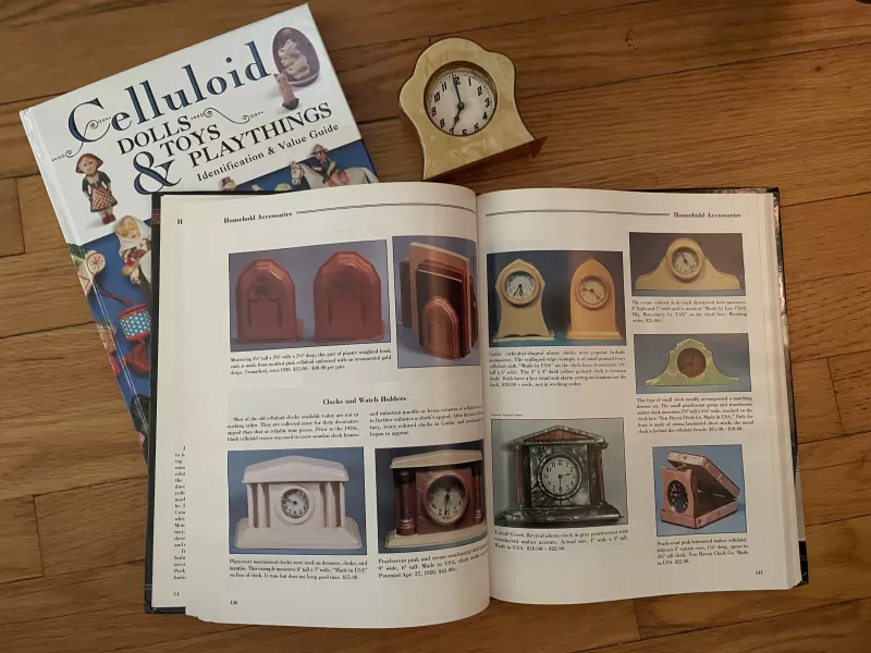 A guide to antiques lays open to pages on clocks, next to another book and an antique clock.