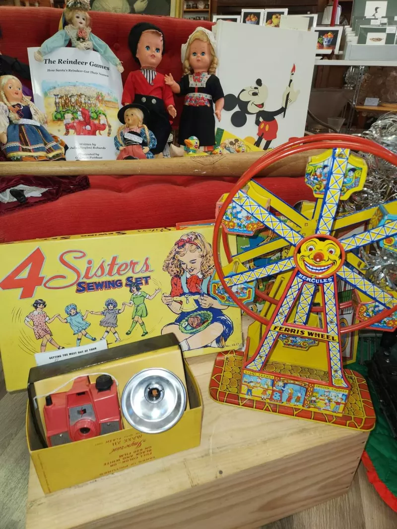 A table of antique toys, including a tin wind-up duck, child's sewing kit, play camera with flash, and tin ferris wheel.