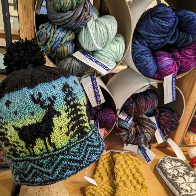 Close-up of a hand-knit winter hat and skeins of all-natural wool on display.