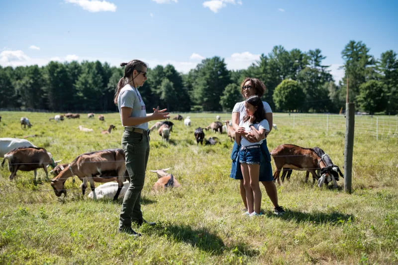 A woman and her daughter listen to a farmhand's lesson about goats.