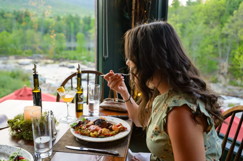 A woman has a drink and a meal by the window of a restaurant.