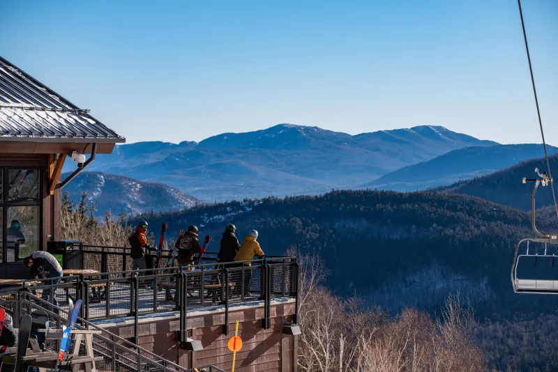A group of skiers look out at a mountain range from a lodge deck.
