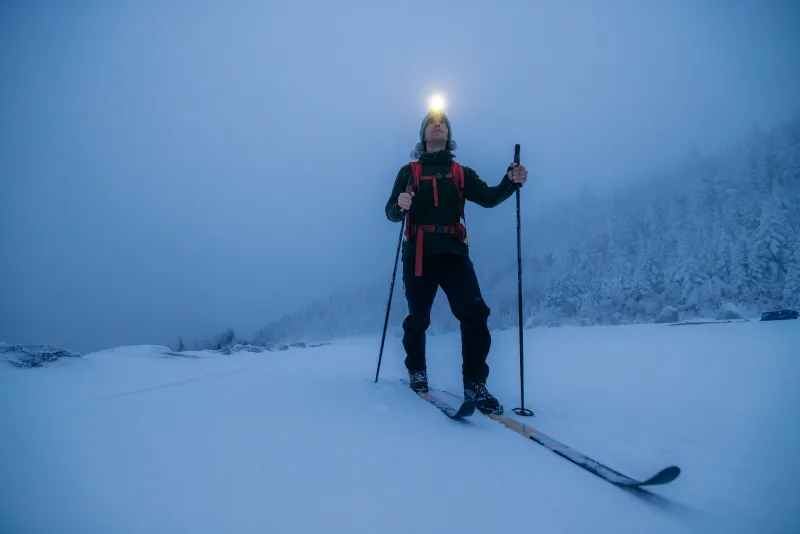 A skier with a headlamp on at dusk