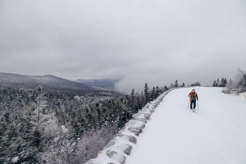 A skier going up a wide road with clouds behind