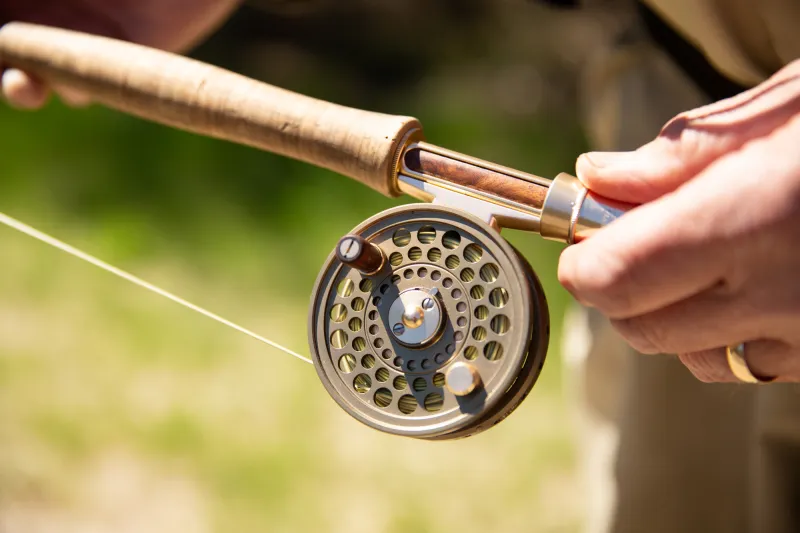 A person's hand holds a fly fishing pole