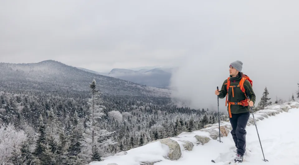 A man cross country skis on a cliffside in winter. 