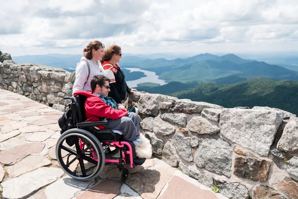 Two ladies and a man in a wheelchair look at the distant mountain views from the summit of Whiteface Mountain.