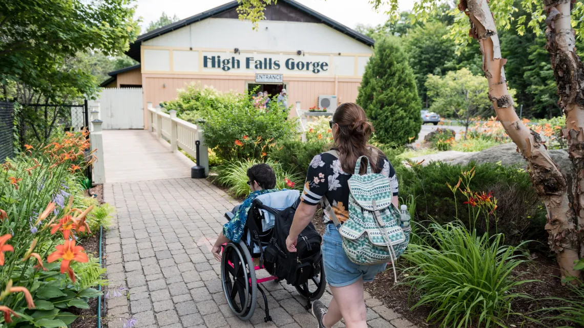 A person pushes another person in a wheelchair on the walkway towards high falls gorge